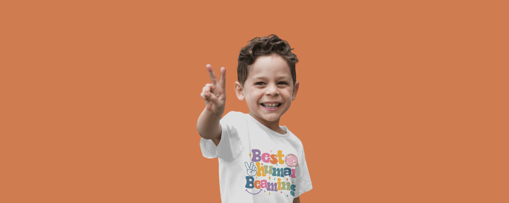 Smiling boy in a white Best Human Beaming t-shirt with a colourful retro logo, holding up a peace sign against an orange background. Fun, empowering, and inclusive kids’ fashion.