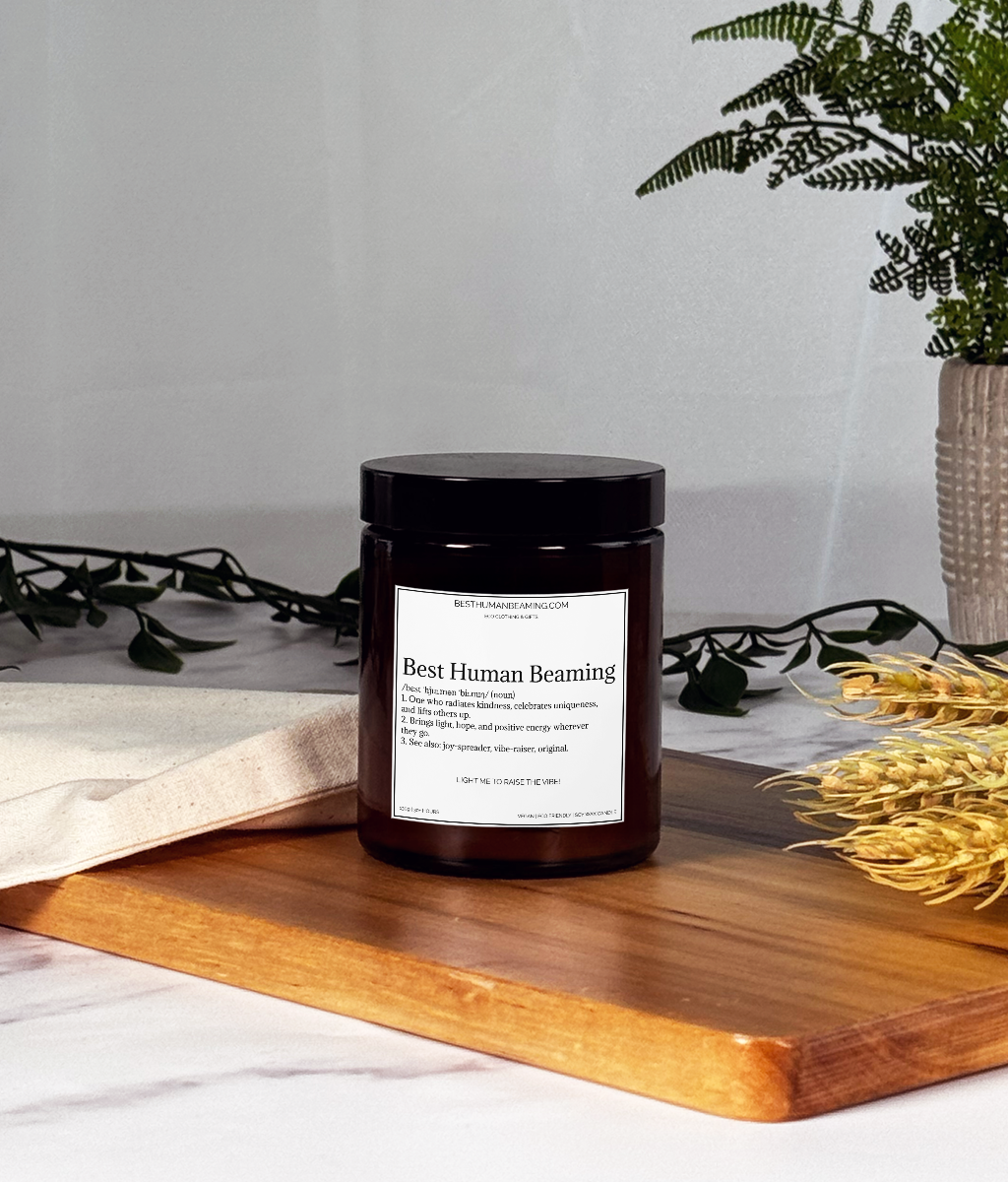 A hand-poured eco-friendly candle in a minimalist glass jar, featuring the Best Human Beaming label. The candle is styled on a clean surface with soft, natural lighting, radiating a warm, inviting glow—perfect for creating a calming and uplifting atmosphere.
