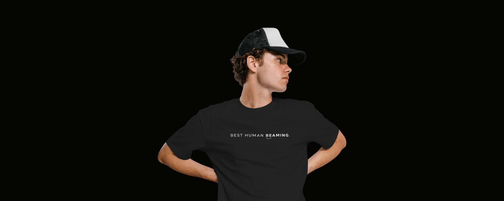 Man wearing a black Best Human Beaming t-shirt with minimalist white logo, paired with a black and white cap. Showcases modern, sustainable, and empowering streetwear style.