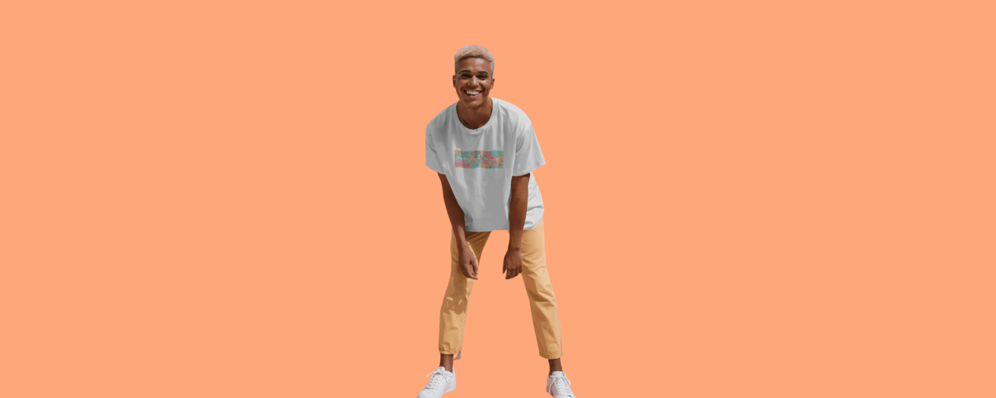 Smiling person in a white Best Human Beaming t-shirt with a colourful abstract print, standing against a peach background. Showcases playful, sustainable, and inclusive fashion.