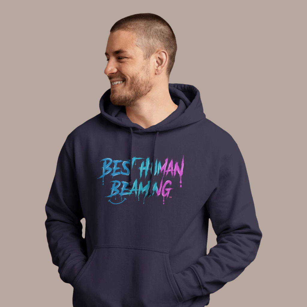 Man in a navy Best Human Beaming hoodie with blue and pink graffiti-style logo. The relaxed pose and bold design reflect confidence and positivity
