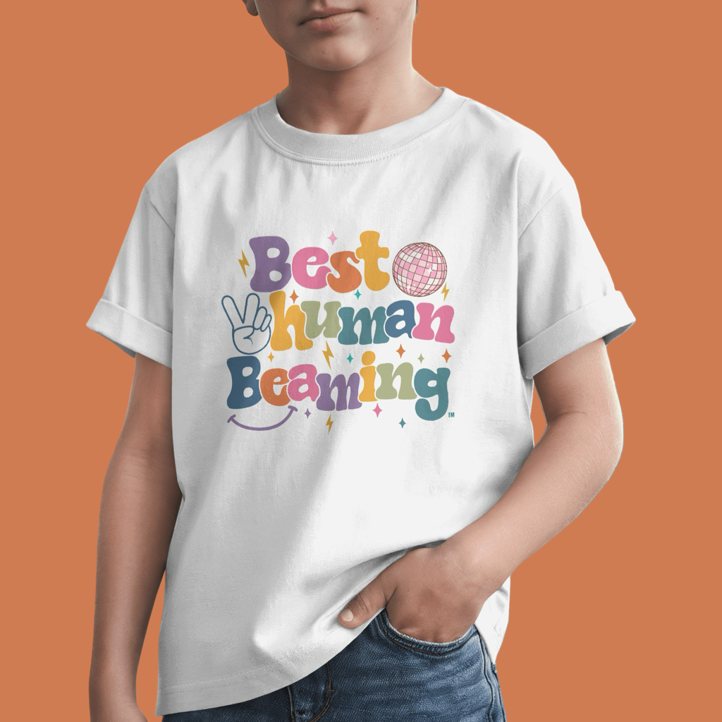 Child in a white Best Human Beaming t-shirt with a colourful retro logo, peace sign, disco ball, and stars. Fun, empowering design for kids on an orange background.