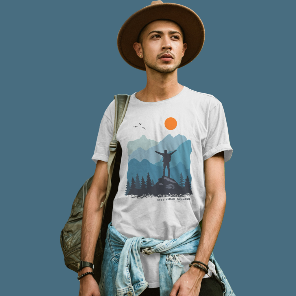 Young man in a white Best Human Beaming t-shirt with a mountain landscape and sun graphic. The design celebrates adventure, empowerment, and nature.