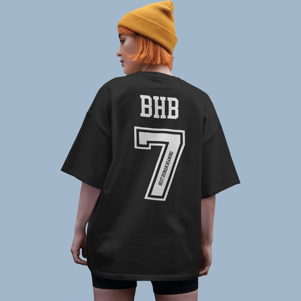 Young woman from behind in a black Best Human Beaming t-shirt with bold “BHB” and a large number 7. The design is sporty and empowering.