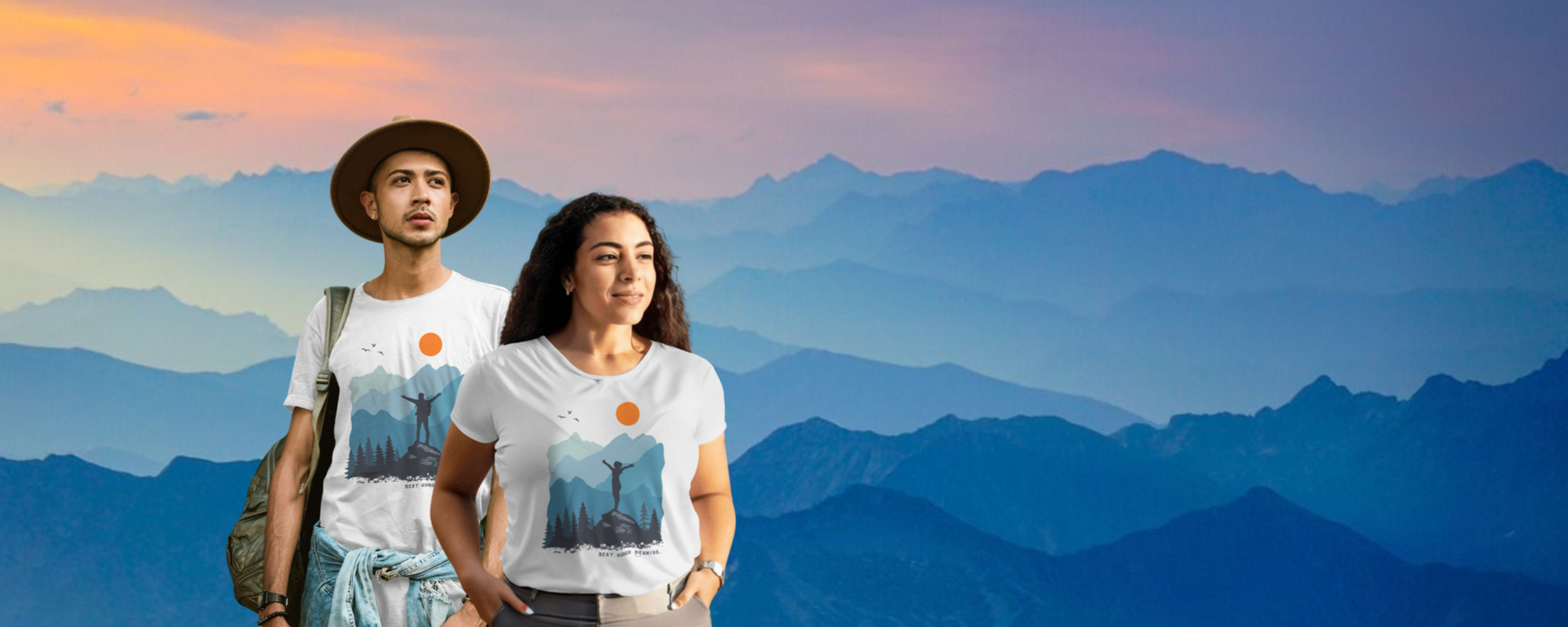 Woman in a white Best Human Beaming Peak Collection t-shirt with mountain and sun design, standing against a blue mountain landscape. Empowering, sustainable fashion for adventurers.
